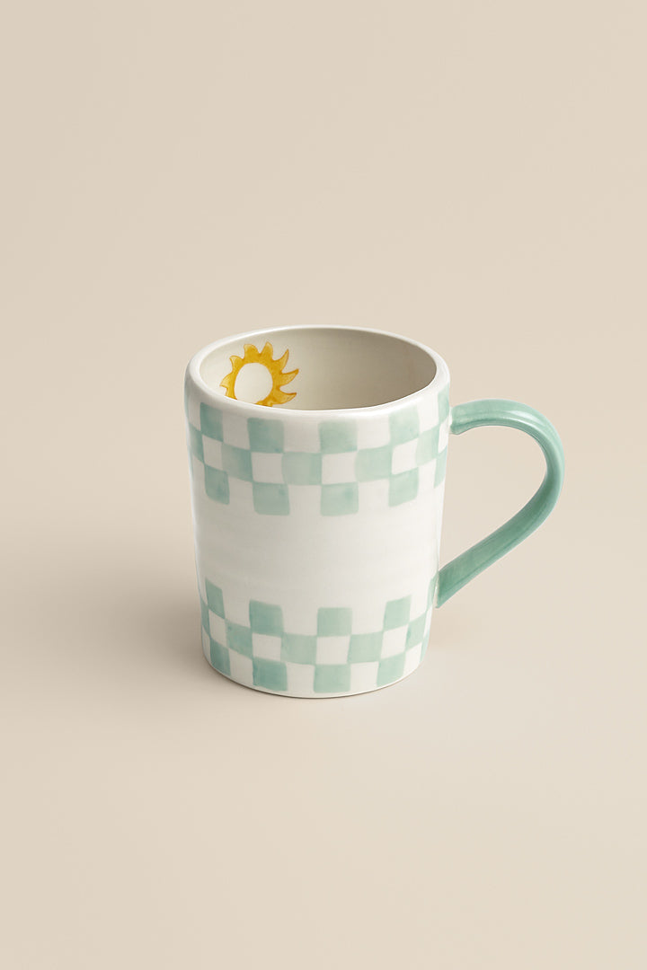 Pale green stoneware mug with checkerboard and sun pattern